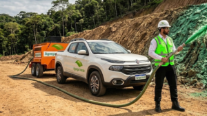 Técnico da Agrega Verde operando hidrossemeador de alta pressão sobre talude erodido, com jato verde de slurry visível no ar