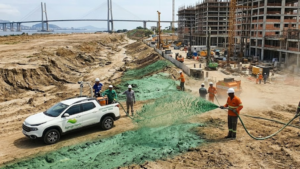Equipe realizando hidrossemeadura em obra de infraestrutura urbana para controle de erosão, revegetação de taludes e recuperação ambiental de área degradada durante construção civil.